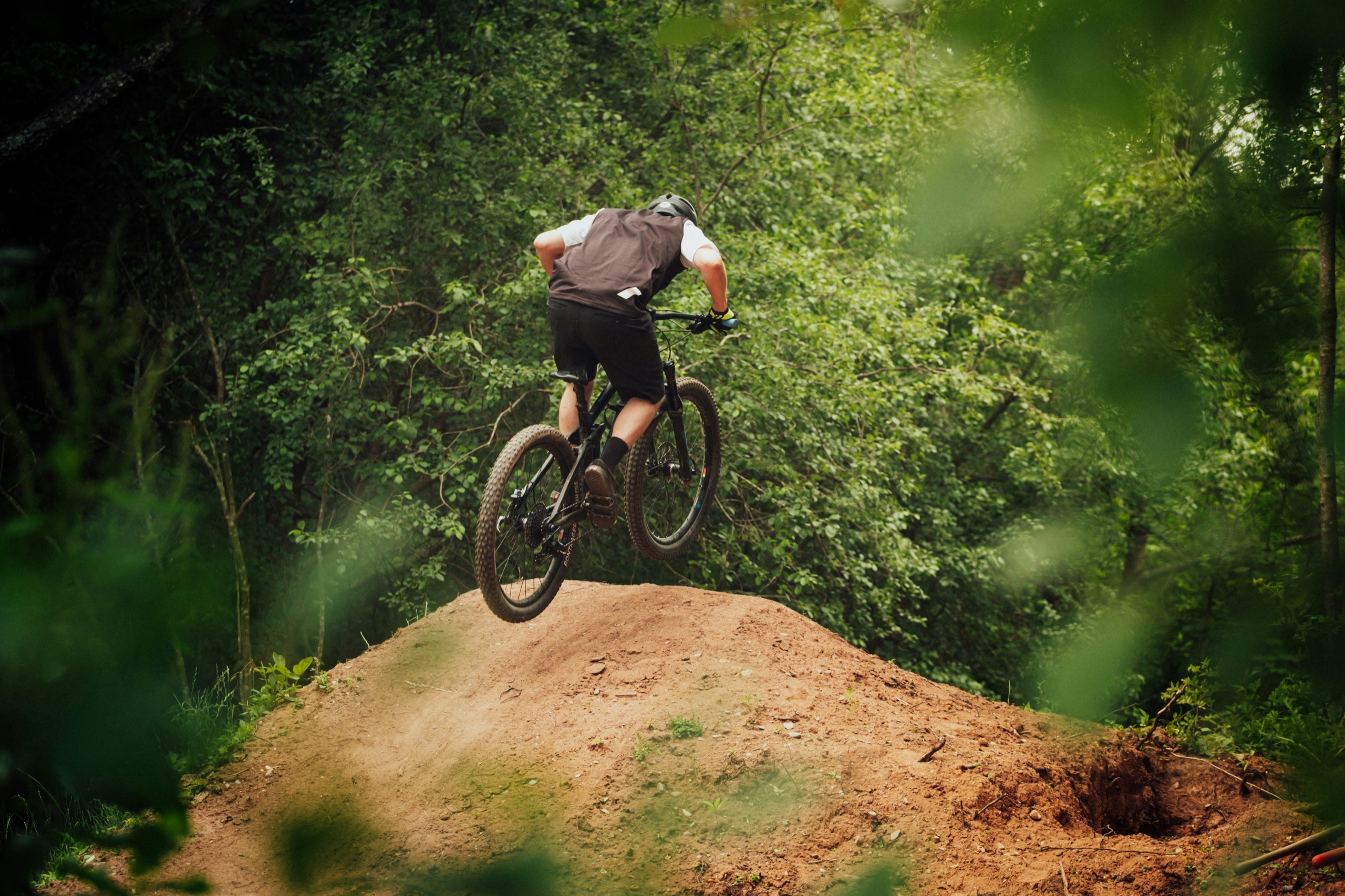 Mountain biker in a black jacket riding a dirt road between green trees